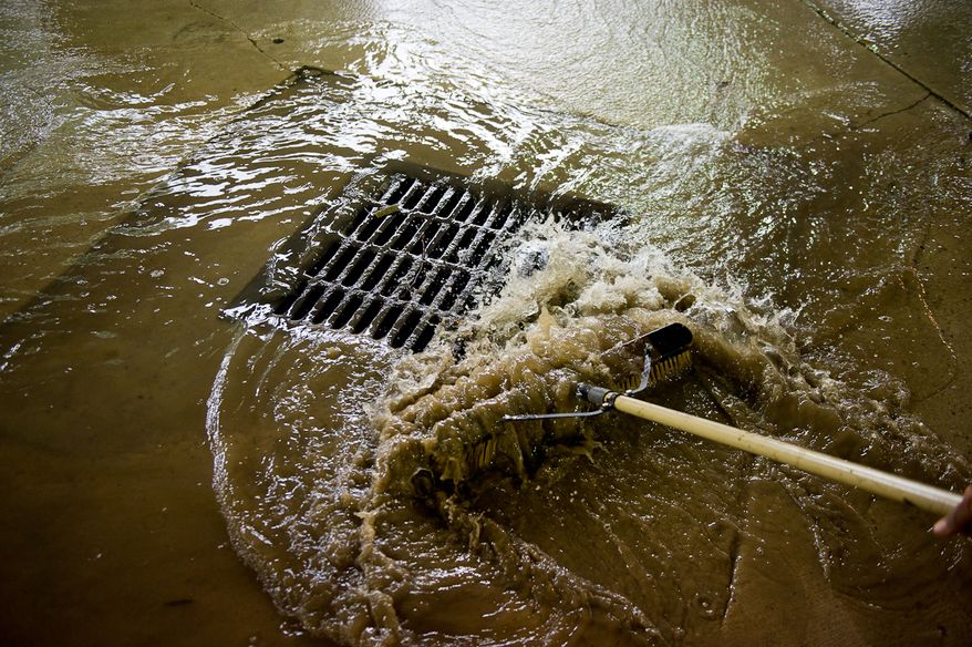 A cleaning crew removes mud from an office building's parking lot on Eisenhower Avenue in Alexandria, Va., on Sept. 9, 2011. The lot was flooded after heavy rains pounded the region the previous night. (Andrew Harnik/The Washington Times)